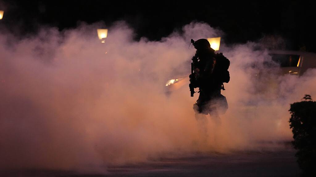 Ein Polizist geht durch Rauch während einer Demonstration gegen die Corona-Impfungen und weiteren Maßnahmen zur Eindämmung der Pandemie. Foto: Petr David Josek/AP/dpa