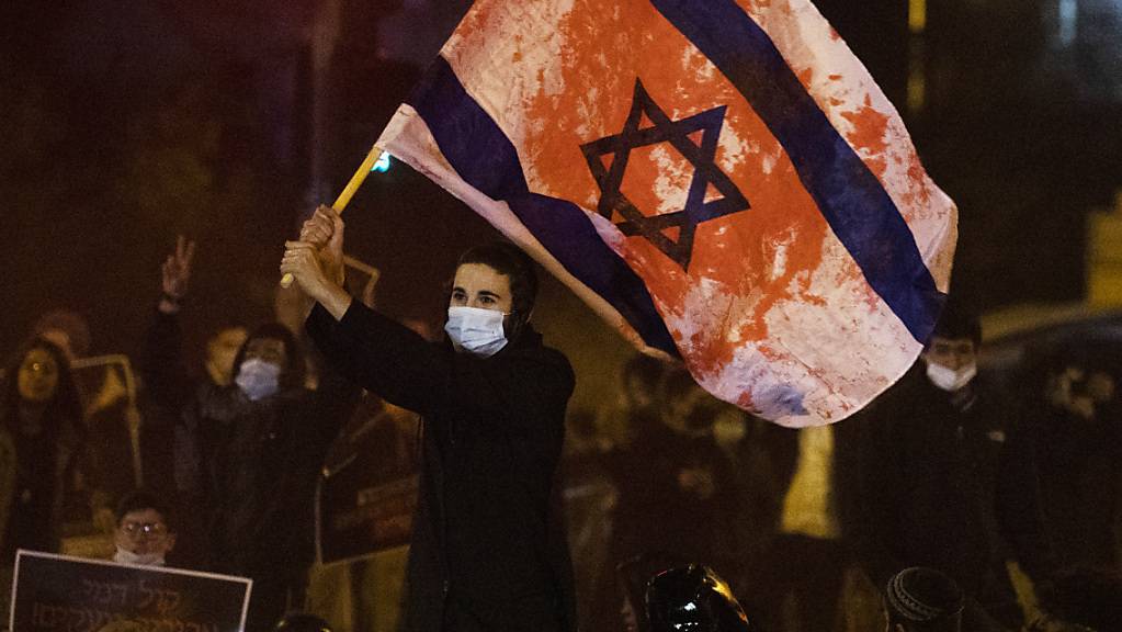 Ein Jugendlicher schwenkt bei einer Demonstration gegen die Polizei eine israelische Flagge, die mit roter Farbe beschmiert ist.