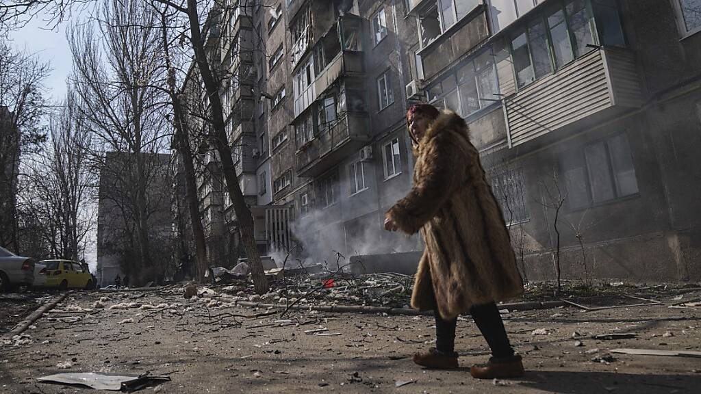 Eine Frau geht an einem brennenden Wohnhaus in Mariupol vorbei. Foto: Evgeniy Maloletka/AP/dpa