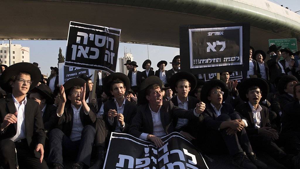 Junge ultraorthodoxe Juden protestieren sitzend auf einer Strasse in Jerusalem gegen die allgemeine Wehrpflicht
