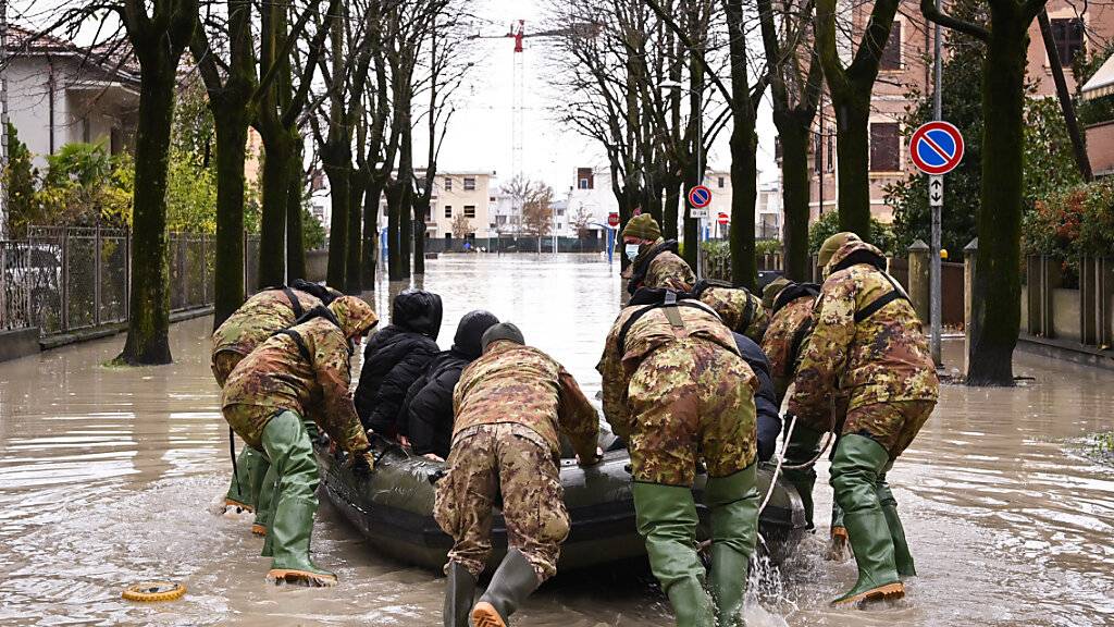 Männer schieben ein Boot inmitten einer überschwemmten Straße in einem Wohngebiet an. Die Wetterlage in Italien bleibt nach heftigen Niederschlägen vom Wochenende angespannt, etliche Familien mussten aus ihren Wohnungen evakuiert werden. Foto: Massimo Paolone/LaPresse via ZUMA Press/dpa