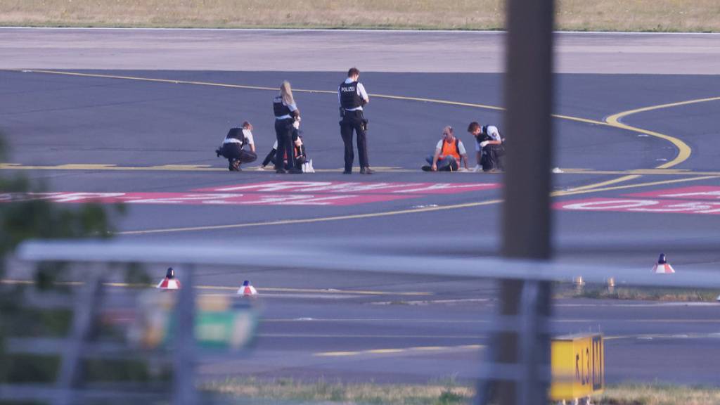 Polizisten stehen auf dem Flugfeld in Düsseldorf (D) und versuchen Aktivisten der Gruppe Letzte Generation vom Asphalt zu lösen, nachdem sie sich festgeklebt haben. (Archivbild)