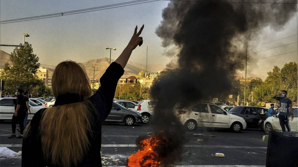 ARCHIV - Eine Frau steht während einer Demonstration in Teheran vor einem brennenden Autoreifen und zeigt das Victory-Zeichen. Foto: Uncredited/AP/dpa/Archivbild