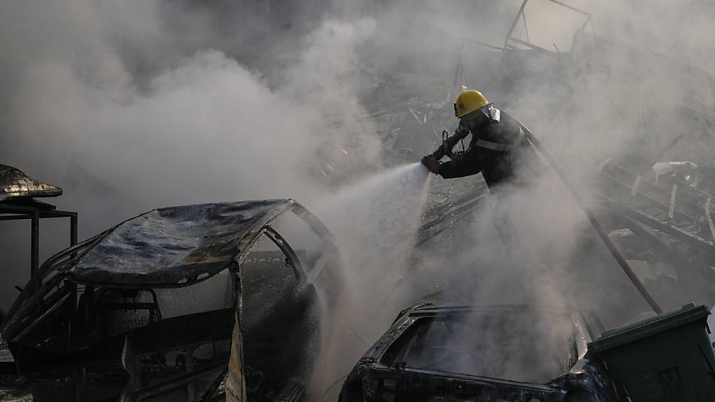 Ein Mitarbeiter des Zivilschutzes löscht ein Feuer, während Rauch vom Ort eines israelischen Luftangriffs aus dem Stadtteil Dahieh, der Hochburg der Hisbollah, aufsteigt. Foto: Hassan Ammar/AP/dpa