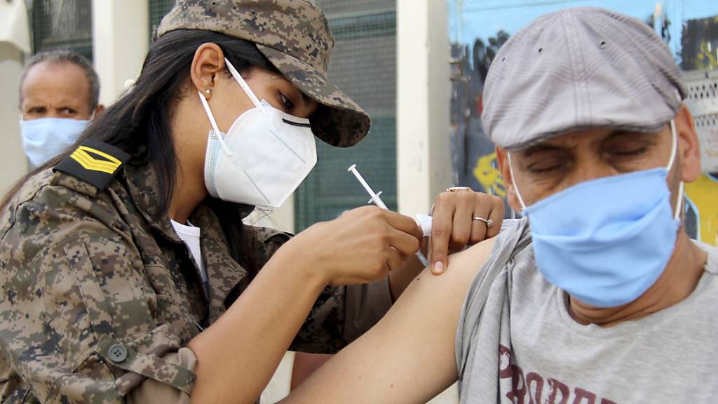 Eine Soldatin verabreicht einem Mann in der Assad-Iben-El-Fourat-Schule den Corona-Impfstoff Vaxzevria während einer Impfaktion. Um die katastrophale Corona-Lage in Tunesien in den Griff zu bekommen, hat eine Impfaktion für bis zu eine Million Bürger im Land begonnen. Foto: Hassene Dridi/AP/dpa