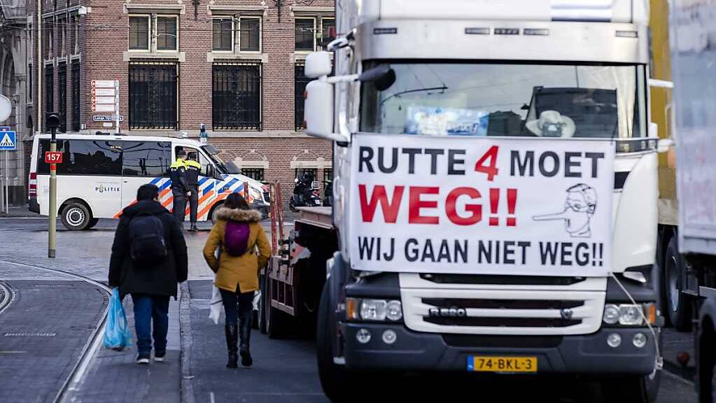 Ein LKW steht auf einer Straße, während im Hintergrund Polizisten eine Kreuzung blockieren. In Den Haag haben am Samstag Lastwagen- und Traktorfahrer aus Protest gegen Corona-Beschränkungen den Zugang zum niederländischen Parlament blockiert. Foto: Sem Van Der Wal/ANP/dpa