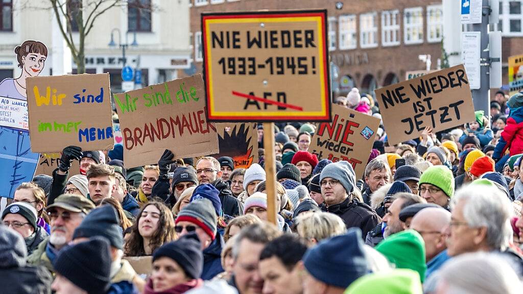 «Nie wieder 1933-1945», «Wir sind die Brandmauer» und «Nie wieder ist jetzt» steht auf Plakaten von Teilnehmern auf der Kundgebung gegen Rechtsextremismus auf dem Platz vor der Stadthalle in Cottbus.