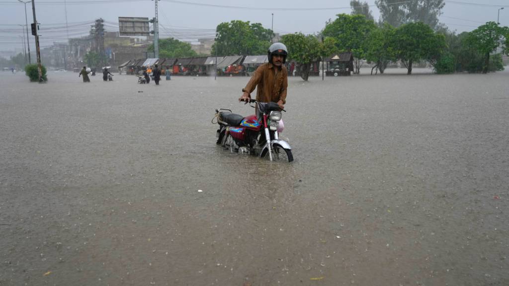 Ein Mann schiebt sein Motorrad über eine von heftigen Monsunregenfällen überflutete Straße. Foto: K.M. Chaudary/AP/dpa