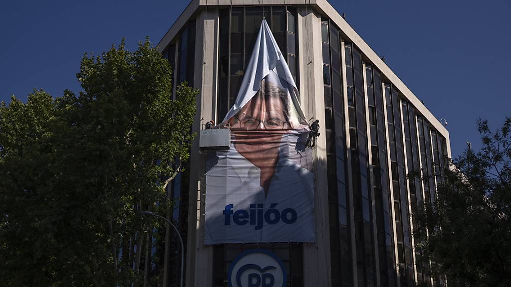 Arbeiter entfernen ein Wahlplakat von dem Vorsitzenden der konservativen Volkspartei Feijoo an der Parteizentrale. Nach der Wahl in Spanien gibt es keinen klaren Sieger. Foto: Emilio Morenatti/AP/dpa