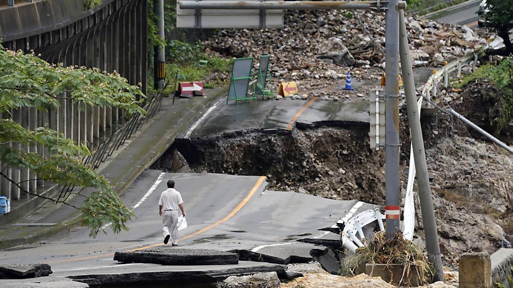 dpatopbilder - Ein Mann geht auf einer stark beschädigten Straße. Rekordstarke Regenfälle hatten am Wochenende schwere Überflutungen und Erdrutsche im Südwesten Japans ausgelöst. Foto: Koji Harada/Kyodo News/AP/dpa