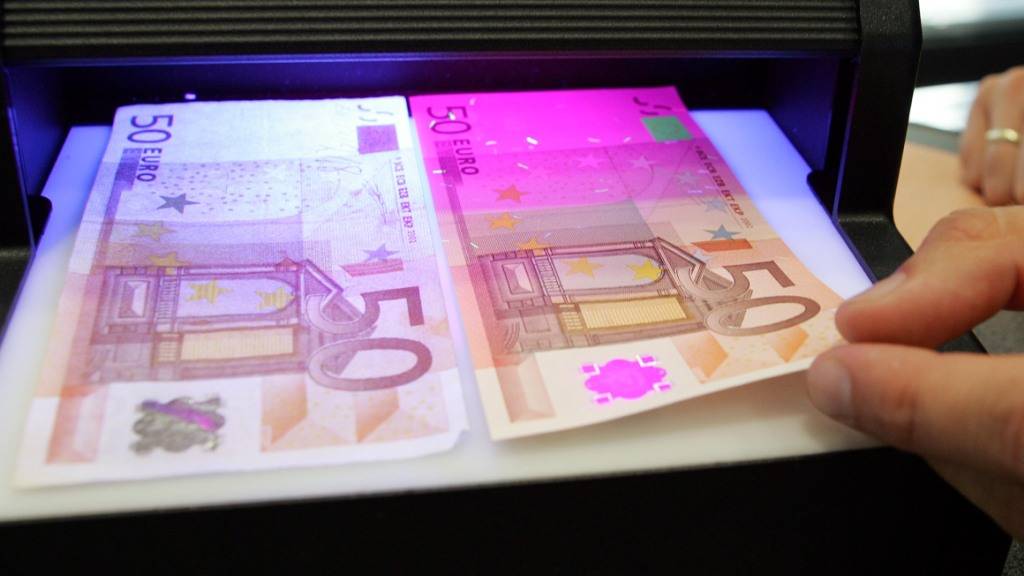 Ein Mitarbeiter der deutschen Bundesbank prüft unter einem UV-Lichtgerät einen falschen (links) und einen echten (rechts) 50-Euro-Schein. (Archivbild)
