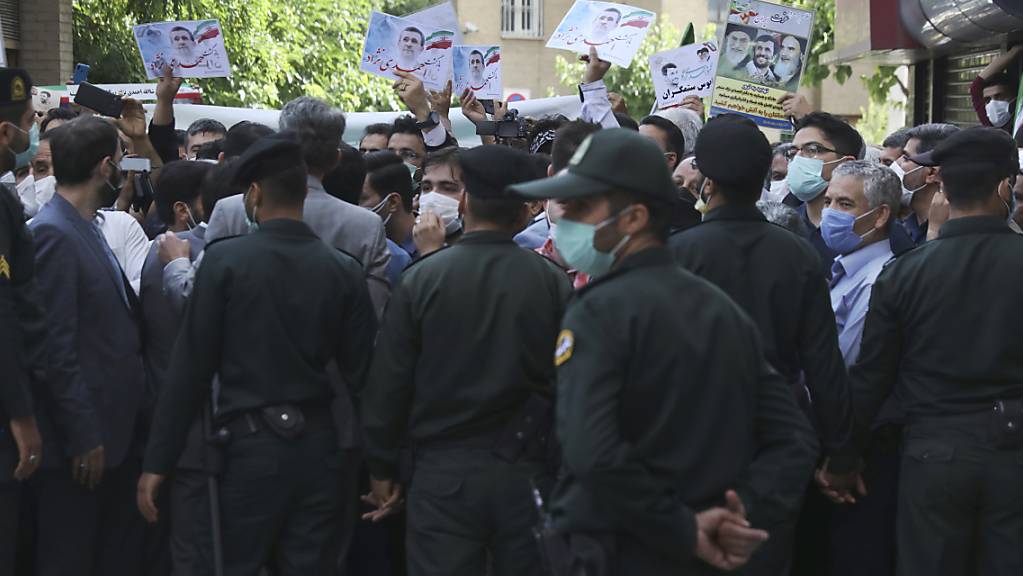 Unterstützer des ehemaligen Präsidenten Ahmadinejad halten Plakate mit seinem Konterfei, während er sich im Innenministerium als Kandidat für die Präsidentschaftswahlen am 18. Juni registriert. Polizisten hindern die Unterstützer daran sich dem Gebäude des Ministeriums zu nähern. Foto: Vahid Salemi/AP/dpa