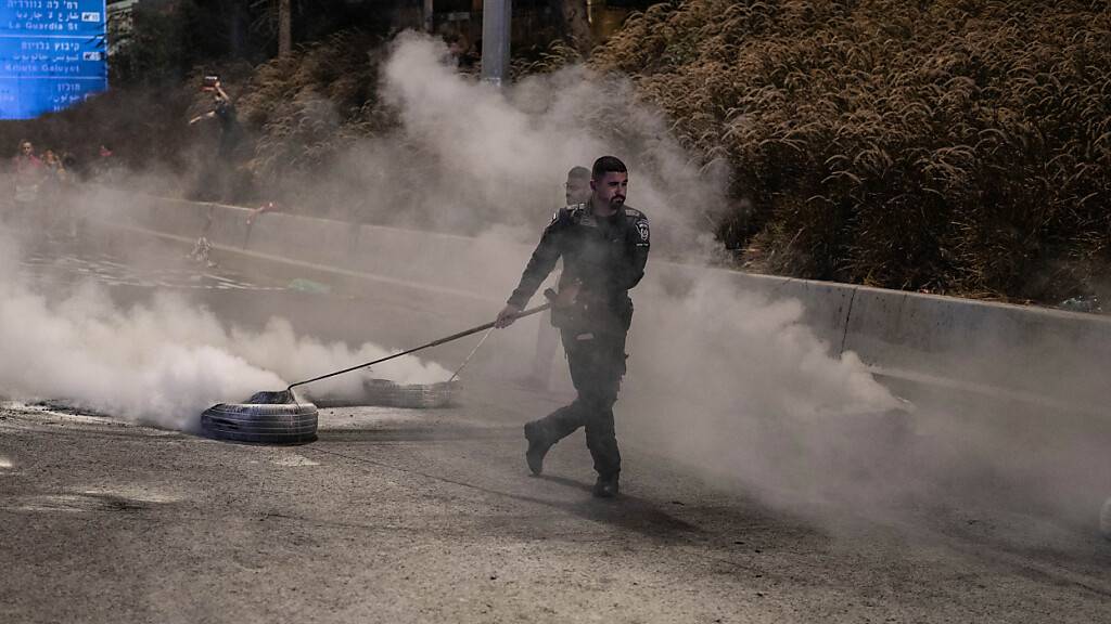 Ein israelischer Sicherheitsbeamter entfernt verbrannte Reifen von der Straße, nachdem die Familien und Unterstützer der von der Hamas entführten israelischen Geiseln versucht hatten, die Hauptstraße am jüdischen Feiertag Jom Kippur zu blockieren. Foto: Ilia Yefimovich/dpa