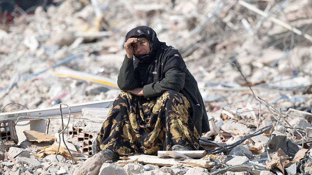 ARCHIV - Eine Frau sitzt zwischen den Trümmern und beobachtet die Bergung von Opfern. Foto: Boris Roessler/dpa
