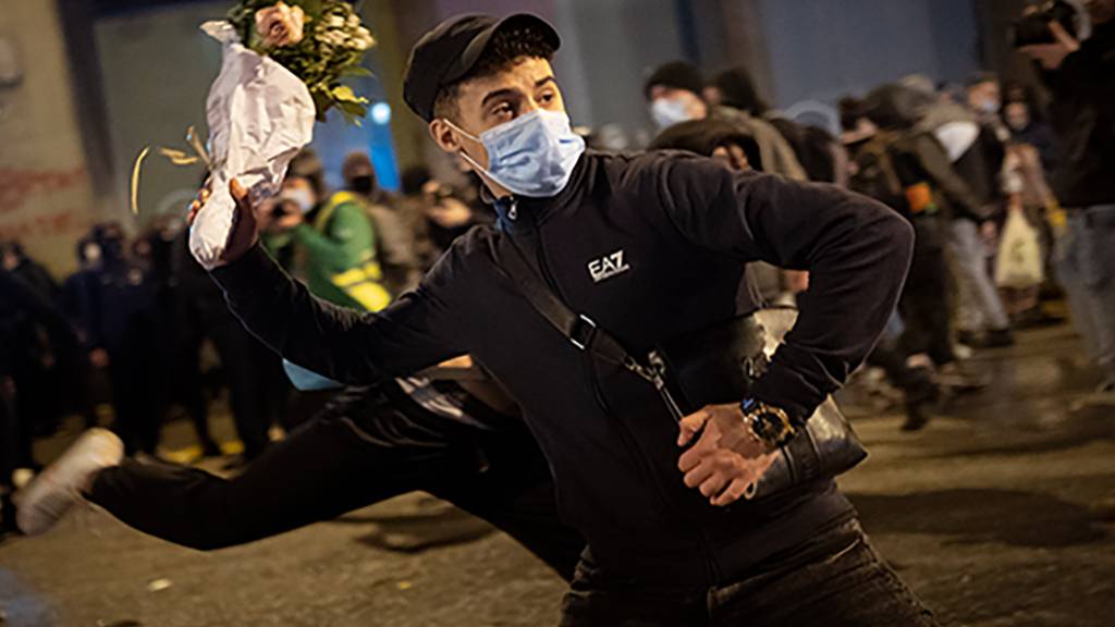 Ein Demonstrant mit Maske wirft einen Blumenstrauß gegen eine nationale Polizeistation während eines Protestes gegen die Inhaftierung des Rappers Hasel wegen Beleidigung des Königshauses. Foto: Emilio Morenatti/AP/dpa