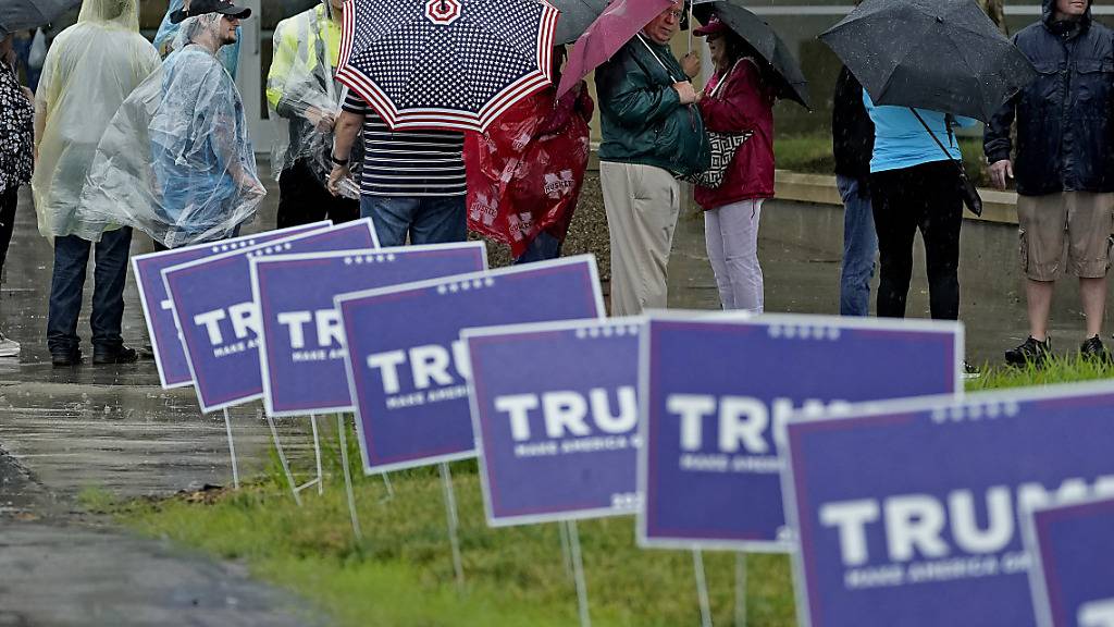 Menschen warten im Regen vor einer Kundgebung mit dem ehemaligen Präsidenten Trump. Foto: Charlie Riedel/AP/dpa