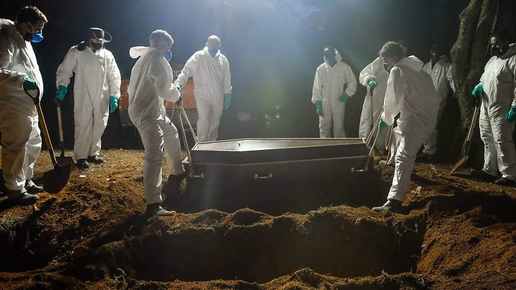ARCHIV - Mitarbeiter des Friedhofs Vila Formosa, dem größten in Lateinamerika, tragen einen Sarg, um eine an Covid-19 verstorbene Person zu beerdigen. Aufgrund der hohen Sterbefälle, arbeiten die Mitarbeiter auch während der Nacht. Foto: Lincon Zarbietti/dpa
