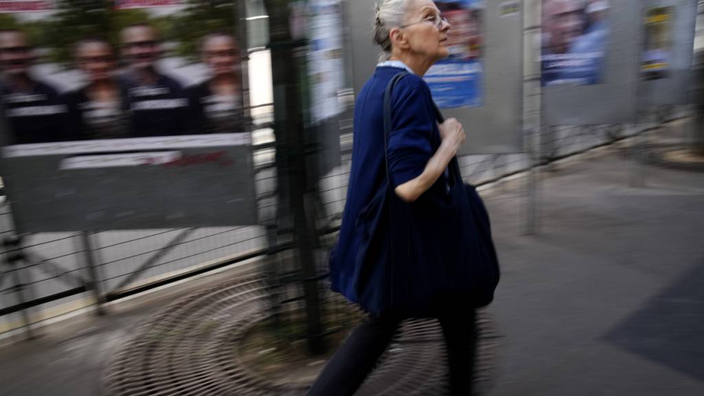 ARCHIV - Eine Frau geht an Wahlplakaten für die bevorstehenden Parlamentswahlen vorbei. In Frankreich könnte es schon bald erneut zu vorgezogenen Parlamentswahlen kommen. Foto: Christophe Ena/AP/dpa
