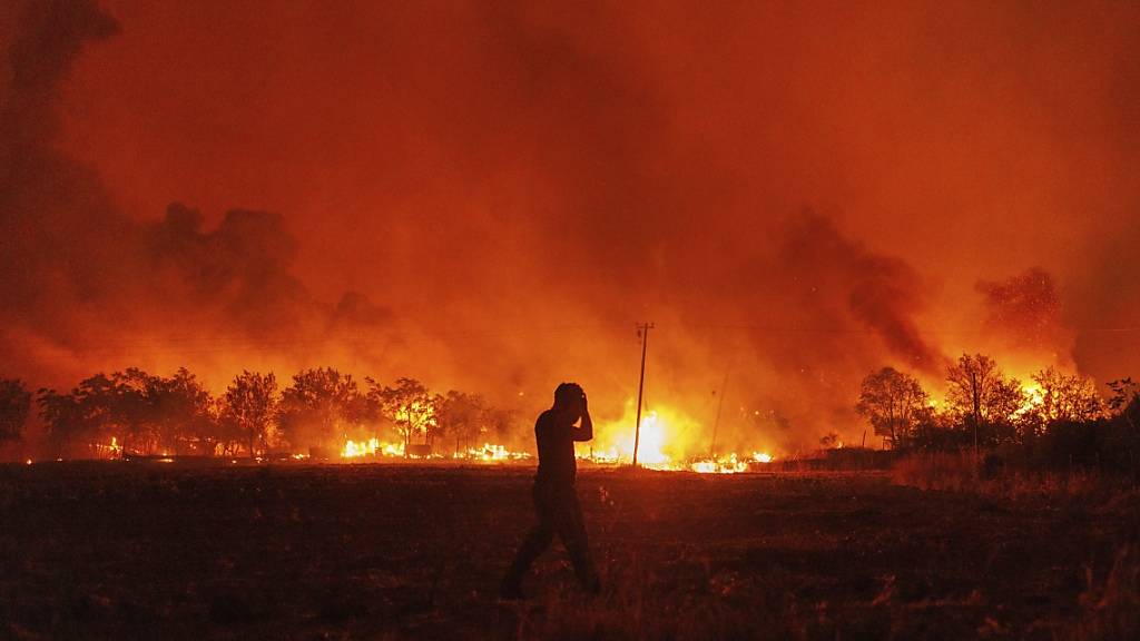 Eine Person geht vor der Kulisse eines Waldbrandes im Dorf Avantas in der Nähe der Stadt Alexandroupolis. Foto: Achilleas Chiras/AP/dpa
