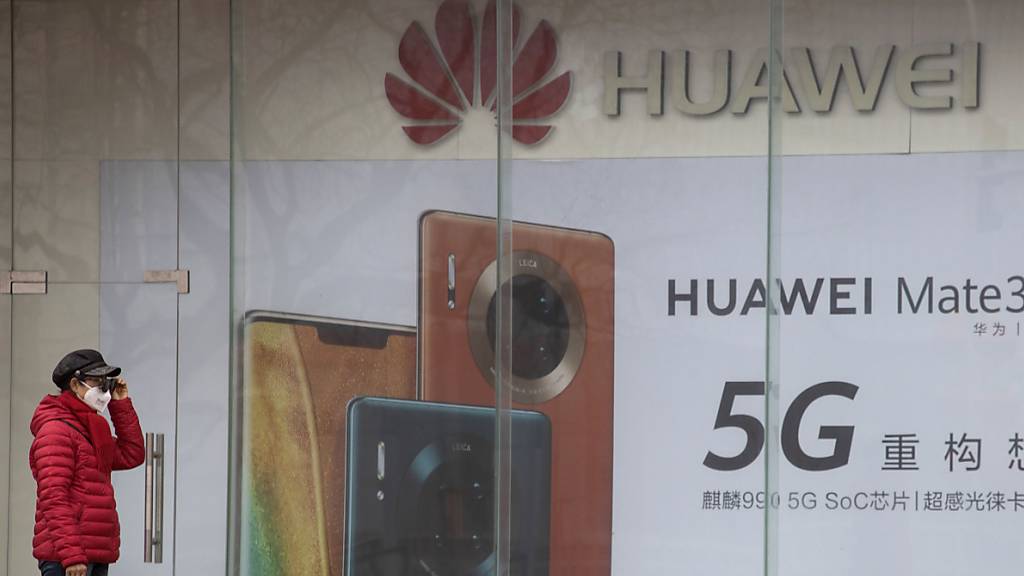 ARCHIV - Eine Frau mit Mundschutz steht vor einer Werbung für Smartphones von Huawei. China hat zwei festgehaltene Kanadier offiziell wegen Spionagevorwürfen angeklagt. Foto: Ng Han Guan/AP/dpa