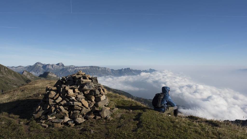 Ein Mann sitzt auf dem Alvier, unten im Nebelmeer das St. Galler Rheintal, im Hintergrund der Alpstein mit Säntis.