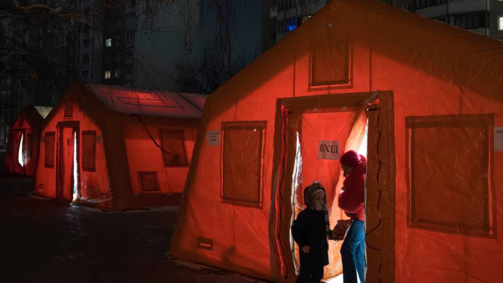 dpatopbilder - Menschen stehen im Eingangsbereich eines Zeltes, das in einem Wohnviertel aufgestellt wurde und in dem sie sich aufwärmen können, nachdem russische Luftangriffe wiederholt Energieinfrastruktur des Landes getroffen haben. Foto: Vladyslav Musiienko/AP/dpa