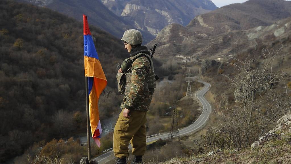 ARCHIV - Ein armenischer Soldat steht neben der Flagge von Berg-Karabach auf einem Hügel in der Nähe von Charektar in der separatistischen Region Berg-Karabach an der neuen Grenze zum Bezirk Kalbajar, der an Aserbaidschan übergeben wurde. Foto: Sergei Grits/AP/dpa