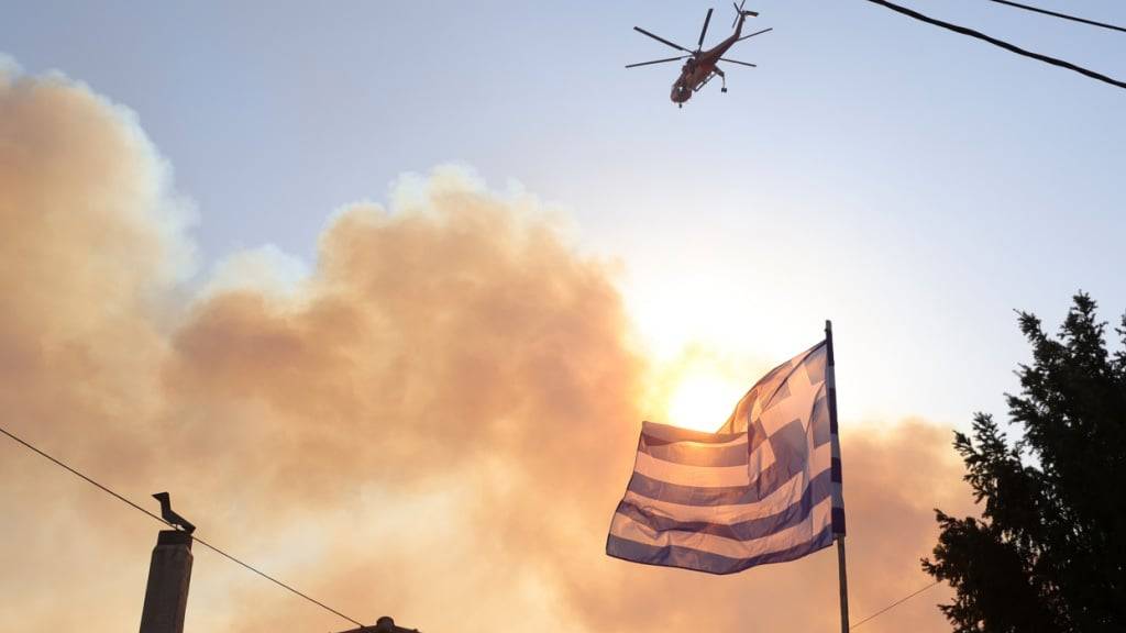 dpatopbilder - Ein Hubschrauber fliegt über ein brennendes Gebiet während eines Waldbrandes im nordwestlichen Vorort Kryoneri. Foto: Yorgos Karahalis/AP/dpa