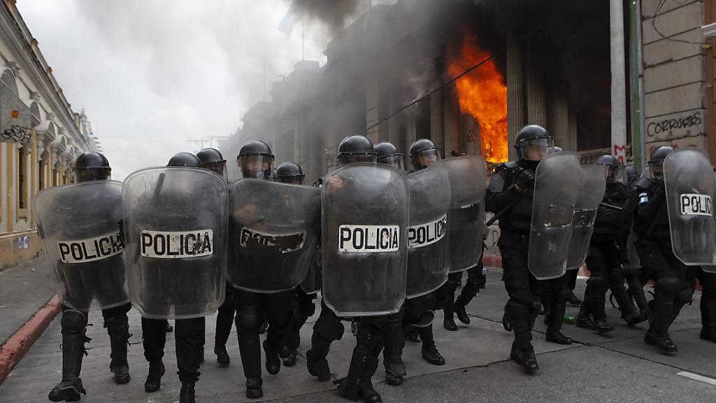 Polizisten bilden eine Blockade gegen Demonstranten. Bei Protesten gegen den Haushalt 2021 haben Demonstranten Teile des Kongresses in Brand gesteckt. Foto: Oliver De Ros/AP/dpa