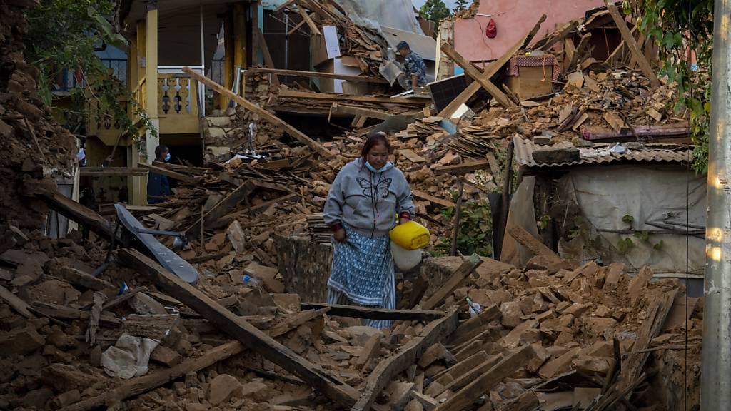ARCHIV - Eine Frau geht an erdbebengeschädigten Häusern im Nordwesten Nepals vorbei. Foto: Niranjan Shrestha/AP/dpa