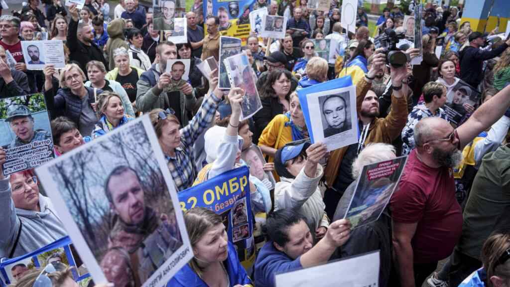 ARCHIV - Menschen halten Fotos ihrer vermissten Verwandten in der Hand, als ukrainische Soldaten während eines Kriegsgefangenenaustauschs zwischen Russland und der Ukraine aus der Gefangenschaft zurückkehren. Foto: Evgeniy Maloletka/AP/dpa/Archivbild