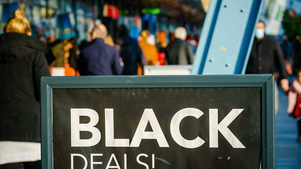 Passanten gehen vor einem Einkaufszentrum an einem Schild vorbei, das auf «Black Friday»-Angebote hinweist. Menschenmassen in Einkaufsstraßen und drohende Verstöße gegen Corona-Regeln: In den Niederlanden lehnen sich Städte gegen die Verkaufsaktion «Black Friday» auf. Foto: Marco De Swart/ANP/dpa