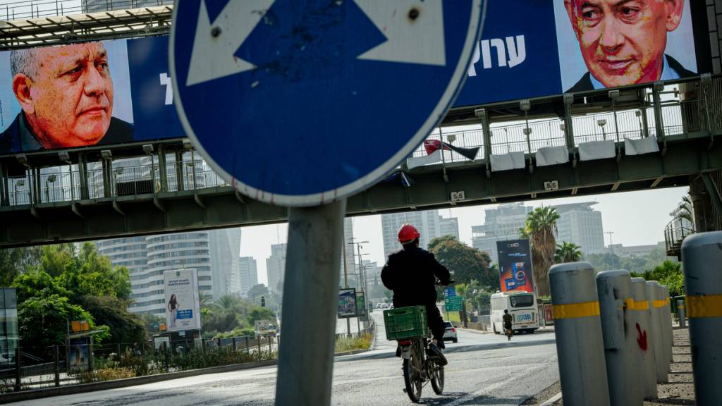 ARCHIV - Ein Radfahrer fährt unter einer Fußgängerbrücke hindurch, an der elektronische Wahlplakate zu sehen sind, auf denen der ehemalige Stabschef der israelischen Streitkräfte, Eisenkot (l), und Ministerpräsident Netanjahu (r) abgebildet sind. Foto: Erik Marmor/dpa/Archivbild