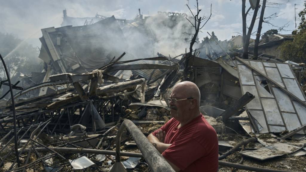 Eine Mann sieht zu, wie Rettungskräfte nach einem Angriff auf die südukrainische Region Odessa an einem zerstörten Gebäude arbeiten. Foto: Libkos/AP/dpa
