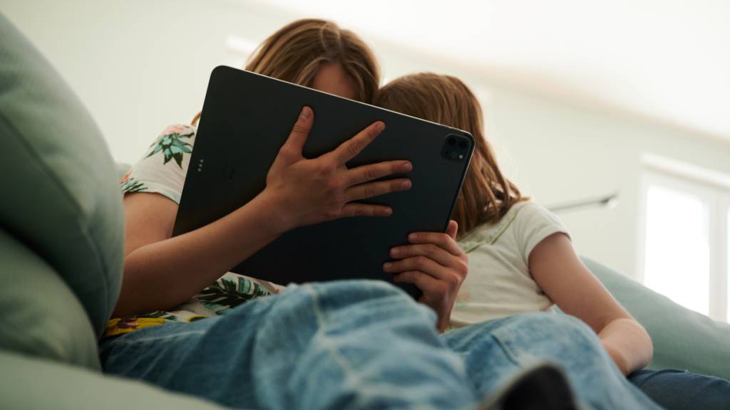 ARCHIV - Zwei Schwestern sitzen auf der Couch und gucken in das Tablet ihrer Eltern. Foto: Annette Riedl/dpa/Symbolbild