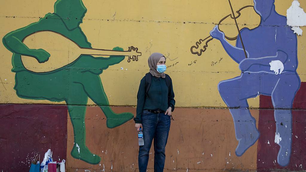 Eine Frau mit Mundschutz wartet vor einer Wand, auf das ein musikalisches Graffiti gemalt ist, auf den Bus. Wenige Tage vor einem Lockdown ist in Israel die Zahl der täglichen Corona-Neuinfektionen erneut auf einen Rekordwert gestiegen. Foto: Ariel Schalit/AP/dpa