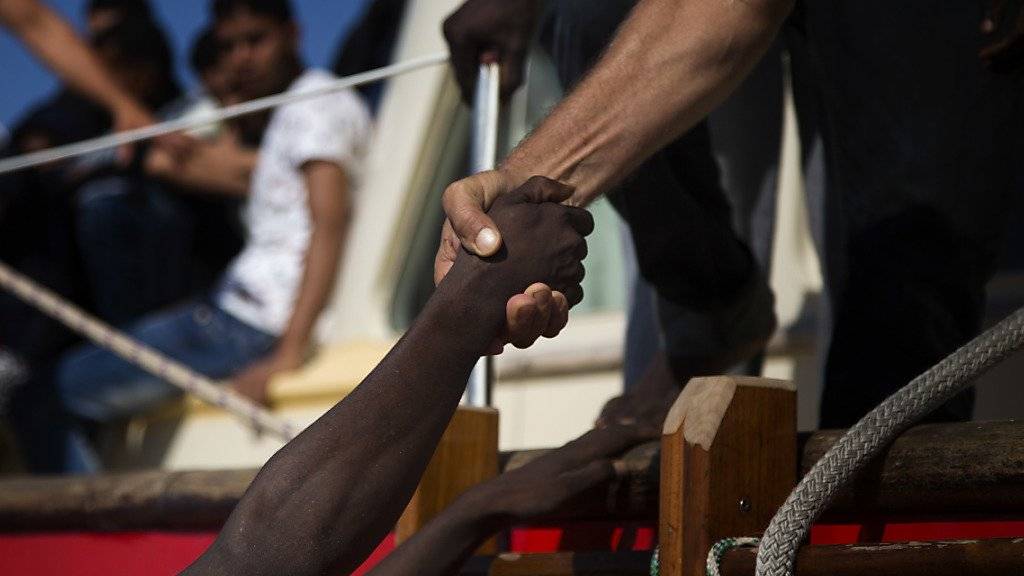 Ein Helfer hilft einem Flüchtling von einem überladenen Boot auf ein Rettungsschiff. (Archiv)