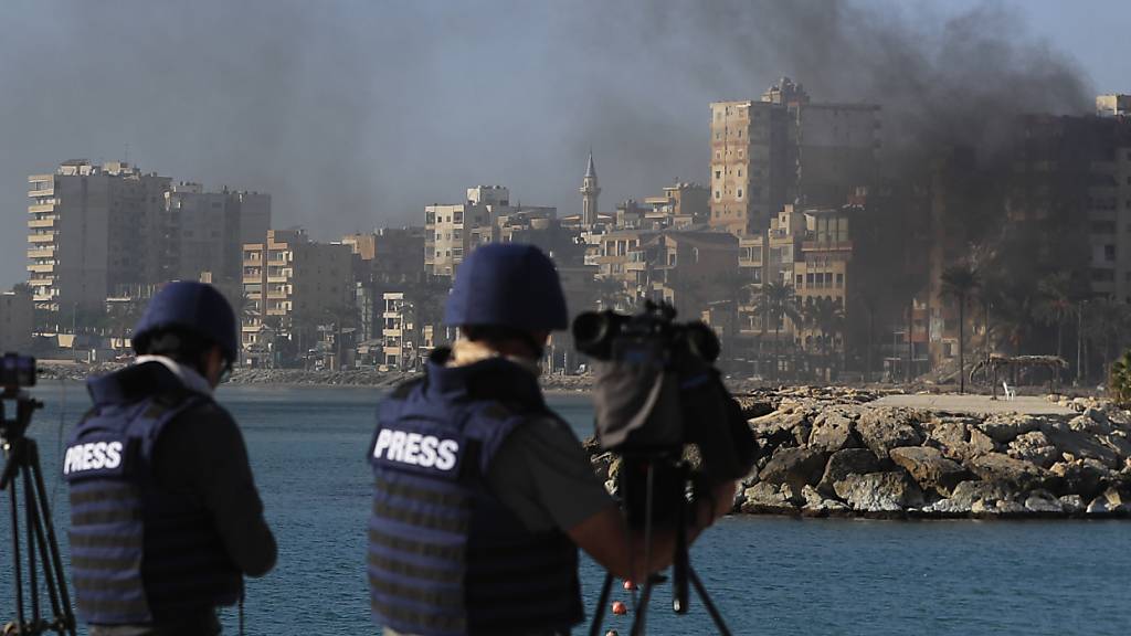 ARCHIV - Journalisten filmen und fotografieren den Ort des Anschlags, wo Rauch von Gebäuden aufsteigt, die bei israelischen Luftangriffen in Tyros im Südlibanon getroffen wurden. Foto: Mohammad Zaatari/AP/dpa