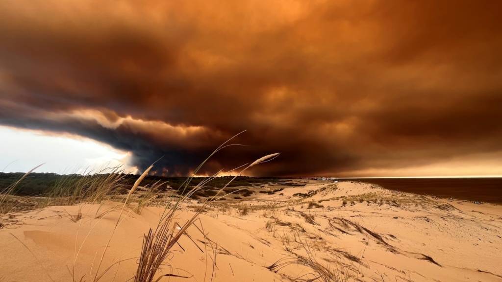 dpatopbilder - Rauchwolken von den Waldbränden südöstlich des Badeortes Lacanau-Ocean (hinten, r) verdunkeln den Himmel, während sie über die Dünen am Nordstrand hinwegziehen. Foto: Jan Athmann/dpa