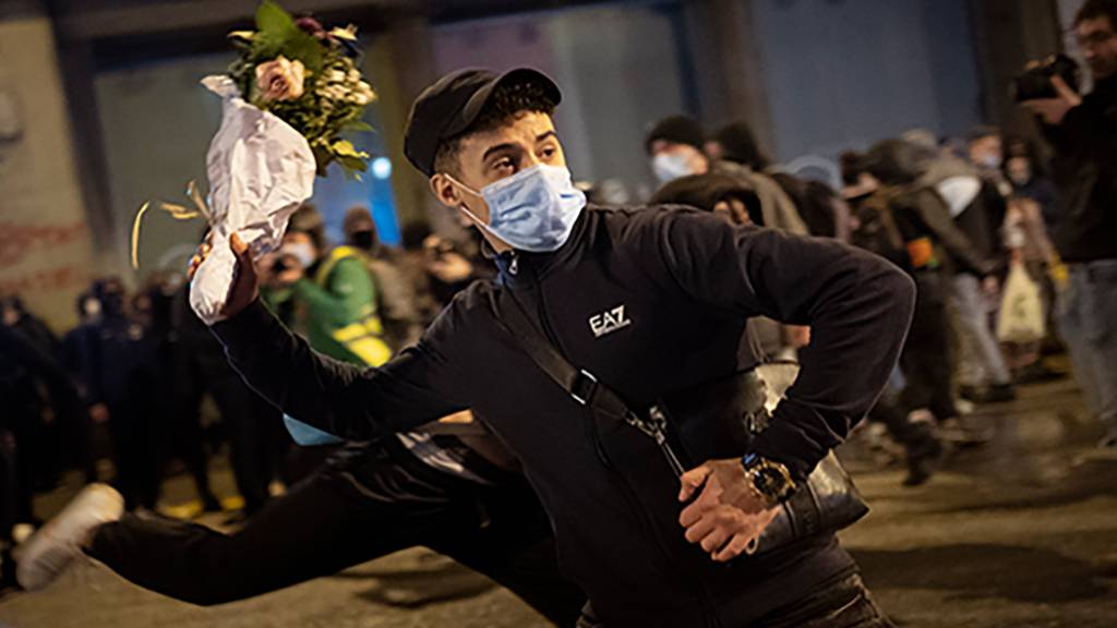 Ein Demonstrant mit Maske wirft einen Blumenstrauß gegen eine nationale Polizeistation während eines Protestes gegen die Inhaftierung des Rappers Hasel wegen Beleidigung des Königshauses. Foto: Emilio Morenatti/AP/dpa