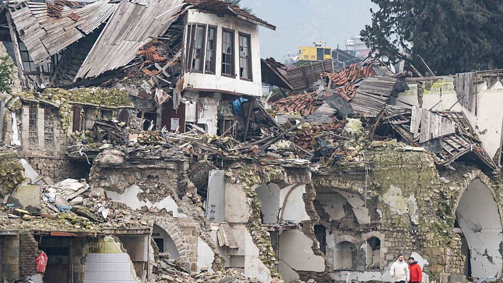 dpatopbilder - Zwei Männer gehen an einer völlig zerstörten Häuserzeile in der Provinz Hatay vorbei. Im Zentrum der Stadt waren bei dem Beben vor einem Jahr unzählige Häuser zerstört oder beschädigt worden. Foto: Boris Roessler/dpa
