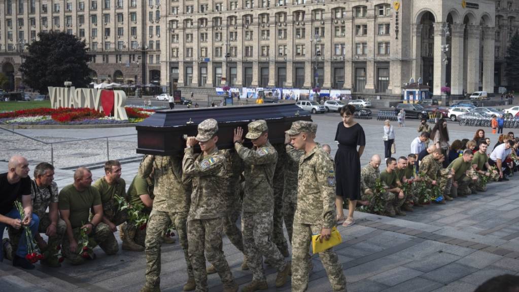 Menschen in Kiew knien nieder, während Soldaten den Sarg eines Kameraden tragen.