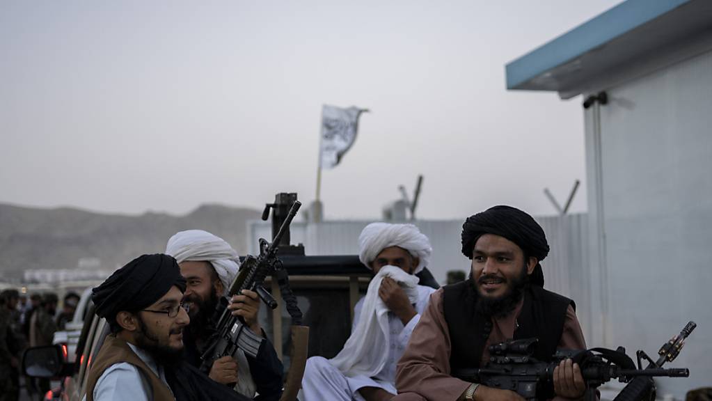 Taliban-Kämpfer sitzen auf der Ladefläche eines Autos auf dem Gelände des Flughafens in Kabul und halten Waffen in ihren Händen.