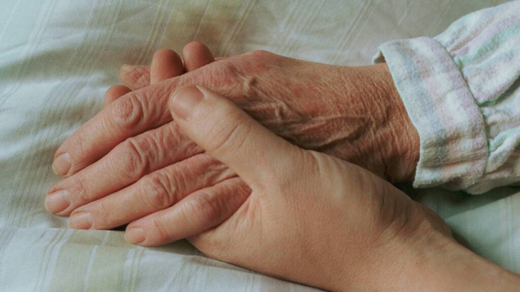 Einer alten Frau wird im Bett die Hand gehalten. (Symbolbild)