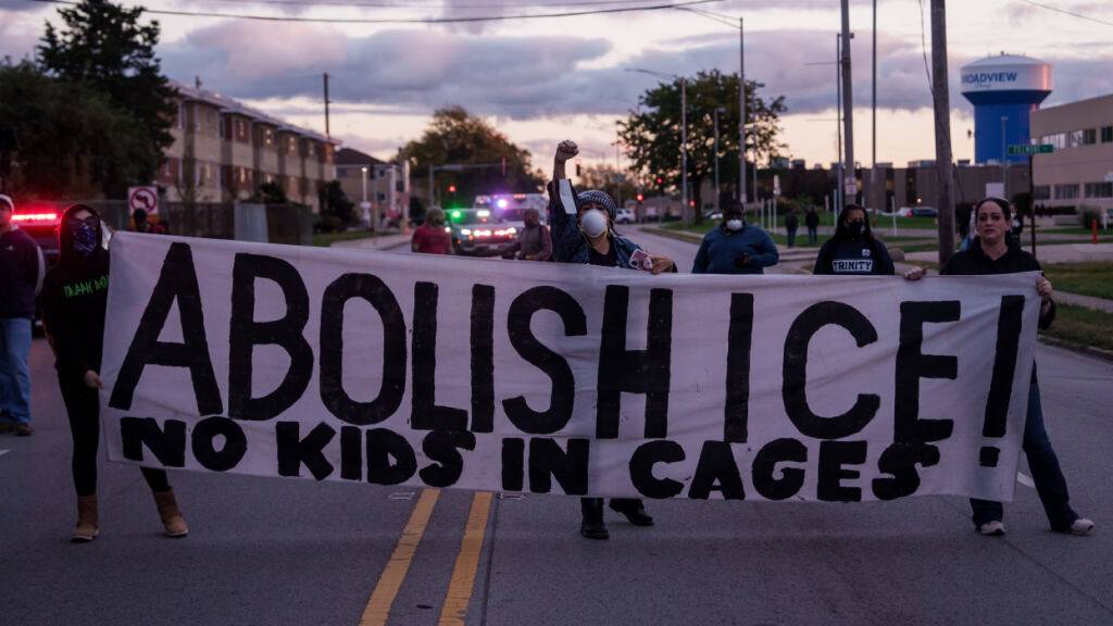 ARCHIV - Menschen halten ein Schild mit der Aufschrift «Abolish ICE» (ICE abschaffen), während die Polizei des Bundesstaates Illinois die Menge zurückdrängt. Foto: Adam Gray/AP/dpa