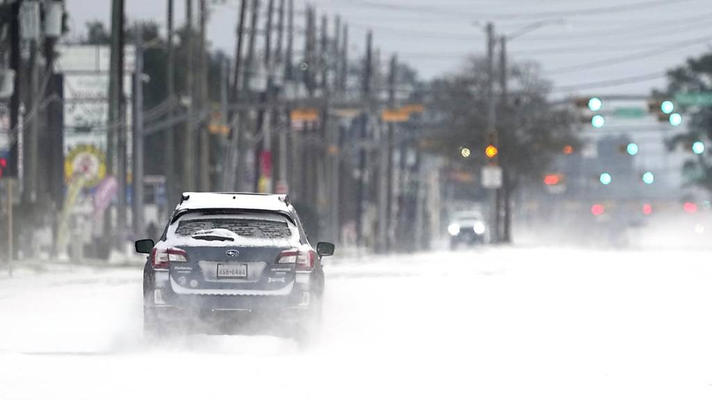 Ein Auto fährt auf einer zugeschneiten Straße. Im südlichen US-Bundesstaat Texas sind wegen ungewöhnlich kalten Winterwetters Hunderttausende Menschen mindestens zeitweise ohne Strom gewesen. Foto: David J. Phillip/AP/dpa