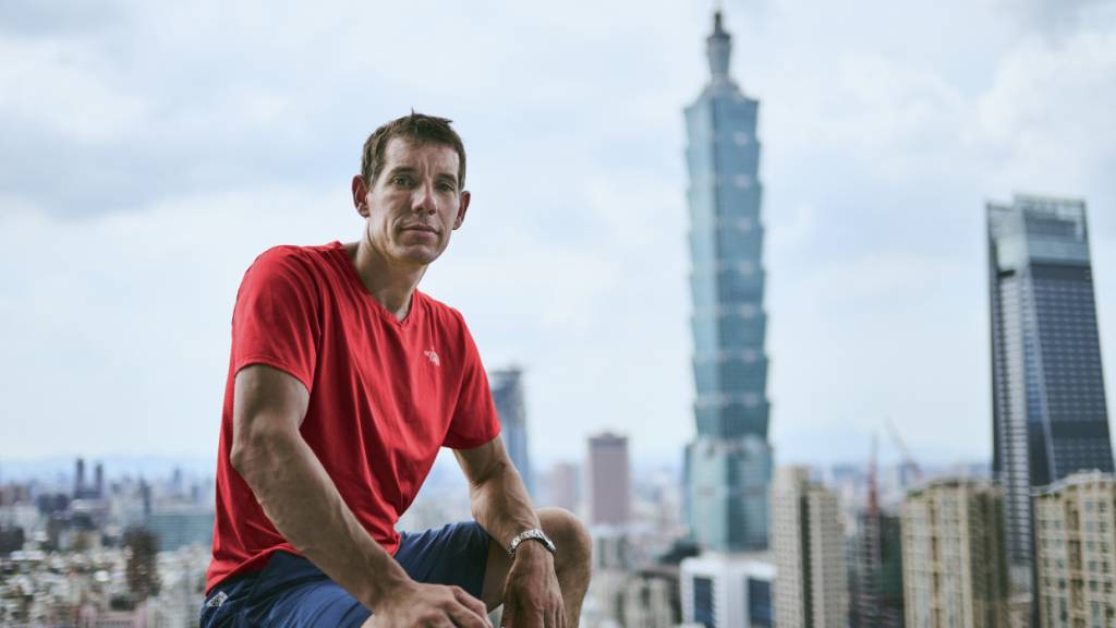 HANDOUT - Alex Honnold sitzt in Taipei auf einem Geländer vor Hochhäusern. In der Nacht auf Samstag (24.01.2026) um 02.00 Uhr (MEZ) will Freeclimber Alex Honnold einen der höchsten Wolkenkratzer der Welt erklimmen, den Taipeh 101. Die Aktion wird live bei Netflix gestreamt. Foto: Corey Rich/Netflix/dpa - ACHTUNG: Nur zur redaktionellen Verwendung im Zusammenhang mit der aktuellen Berichterstattung über den Live-Stream von Netflix und nur mit vollständiger Nennung des vorstehenden Credits