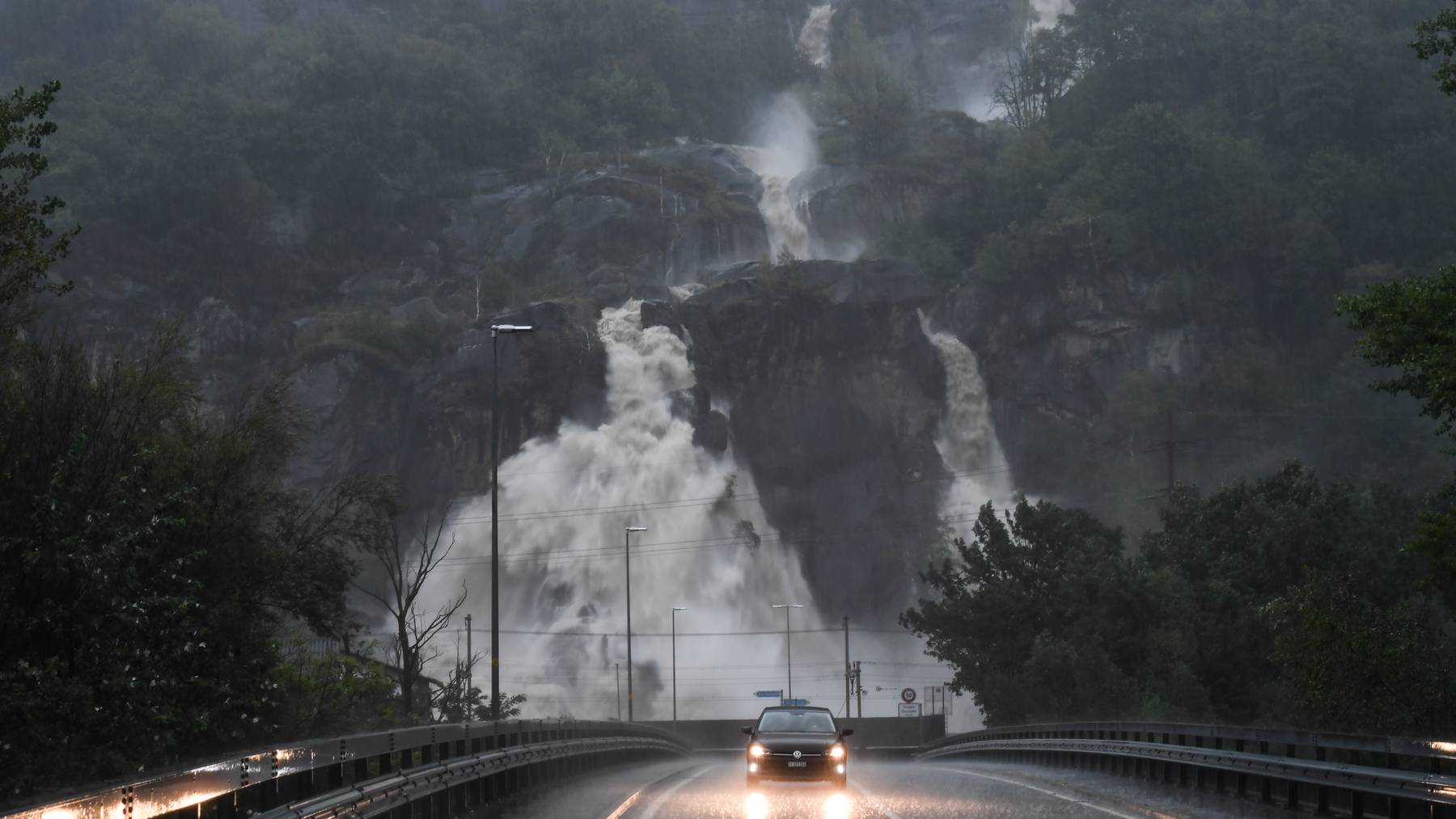 Im Tessin hat es die zweite Nacht in Folge teils äusserst heftig geregnet. Im Bild: Die überflutete Kantonsstrasse bei Cresciano, dahinter Wasserfälle.