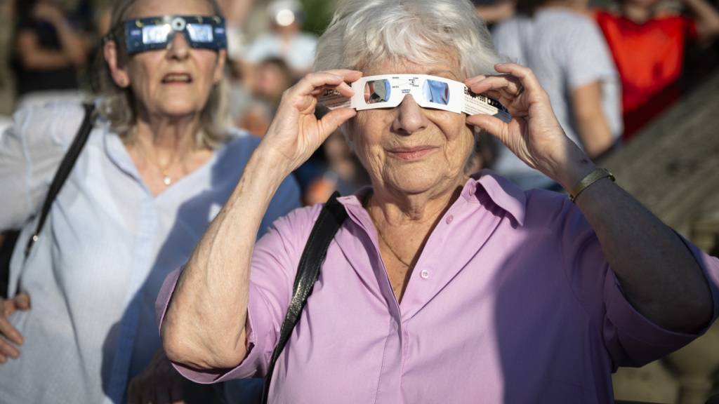 Zwei Frauen beobachten mit Schutzbrillen ausgerüstet am Mittwochabend auf der Zürcher Polyterrasse, wie der Mond die Sonne während der partiellen Sonnenfinsternis verdunkelt.