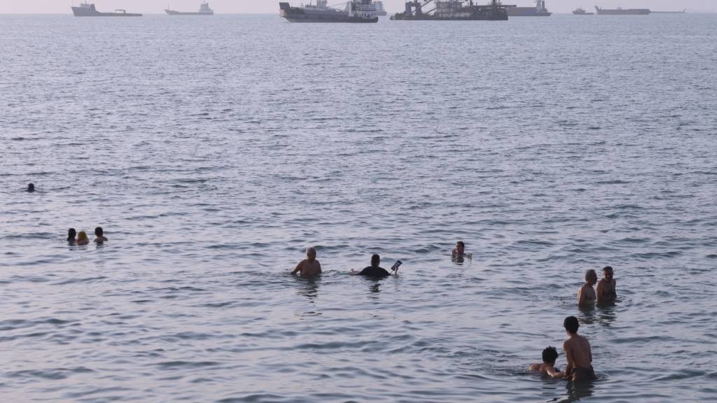 dpatopbilder - Anwohner schwimmen, während Fracht- und Handelsschiffe in der Straße von Hormus vor Bandar Abbas im Iran vor Anker liegen. Foto: Amirhosein Khorgooi/ISNA/AP/dpa